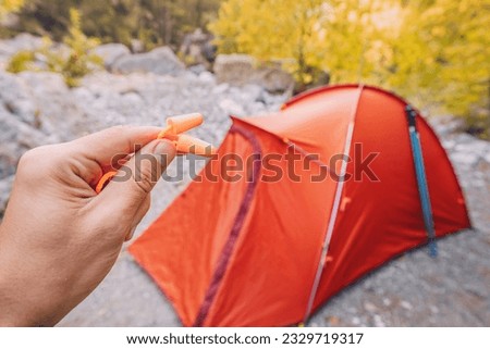earplugs in the hand of a hiker on the background of a camping tent. Insomnia and sleep in nature