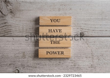 Stack of four wooden pegs with a You have the power sign on them placed over white textured wooden background. 