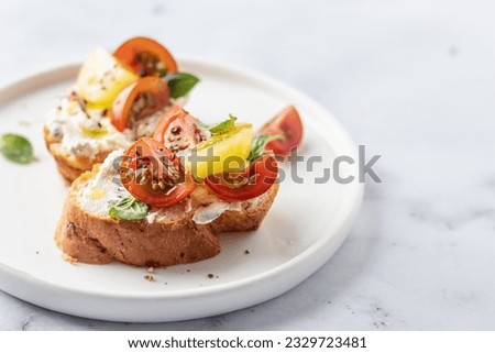 Bruschetta sandwiches with tomatoes, cream cheese, olive oil and basil on a plate on white marble background, copy space. Traditional italian antipasti. Horisontal Royalty-Free Stock Photo #2329723481