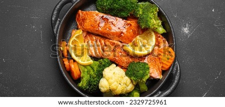Healthy baked fish salmon steaks, broccoli, cauliflower, carrot in cast iron casserole bowl on black dark stone background. Cooking a delicious low carb dinner, healthy nutrition Royalty-Free Stock Photo #2329725961