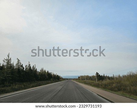 A wide open empty highway through a rural area of New Brunswick on an early spring morning. The road has its pavement ripped up due to repaving taking place.
