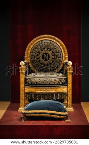 Close-up image of the interior design of Napoleon III's royal apartments and his beautiful throne, sitting on a wooden podium on a red carpet that continues behind the backrest on the wall.  Royalty-Free Stock Photo #2329735081