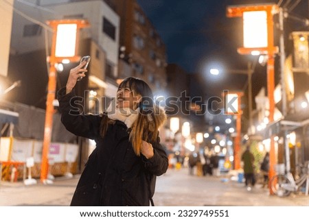 Asian woman using mobile phone taking selfie during travel Sensoji Temple at Asakusa Tokyo, Japan at night. Attractive girl enjoy urban outdoor lifestyle travel city street on winter holiday vacation.
