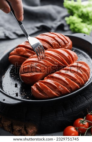 Grilled smoked sausages in pan in dark wooden background with tomatoes and spices. Hot sausage on a fork, meat food, selective focus