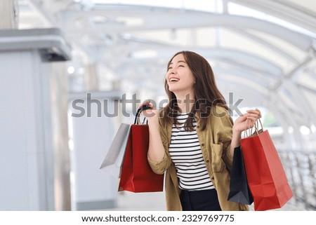 Cheerful Asian woman holding shopping bags.Beautiful Asian woman in casual style shopping in the city. Royalty-Free Stock Photo #2329769775