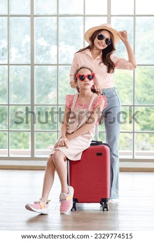 Asian cheerful happy family mom and daughter wearing sunglasses and hat standing posing with red trolley luggages smiling celebrating holiday together ready for traveling vacation weekend road trip.
