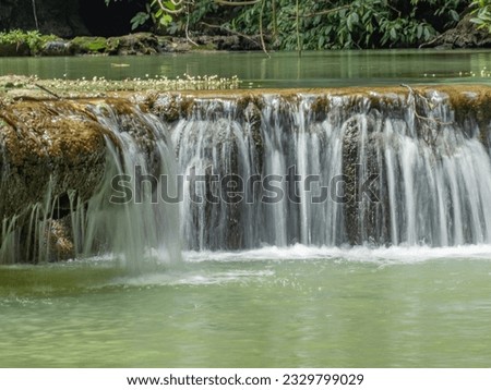 the waterfall flows through the rocks. ripples of water rippling, the water reflects the green of the forest, peaceful, suitable for tourism and relaxation. composition with empty space below.