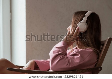 A young beautiful woman listening to music with headphones with her eyes closed sitting on a retro wooden chair.. Peace, harmony, relaxation and relaxation.