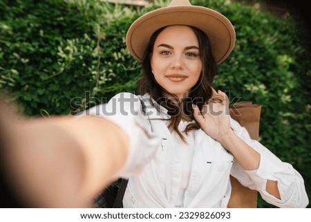 Young smiling woman with shopping bags making selfie walking in a city park at summer day on green background. Copy space