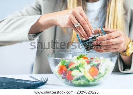 The vibrant flavors of healthy eating at the workplace as a woman indulges in a refreshing salad. With a bowl filled with crisp greens, she adds nutritious seeds, enhancing the taste and nutritional v
