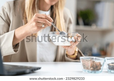 Nutritious meal at work. Woman indulges in a satisfying bowl of muesli and creamy yogurt, fueling her body with a balanced and energizing breakfast Royalty-Free Stock Photo #2329829233