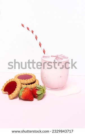 Refreshing strawberry milkshake with biscuits and strawberries on a white and pink background.