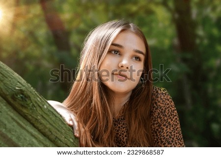 Emotional girl teenager with long hair hairstyle braids in a green shirt sits on a bench in the park. High quality photo
