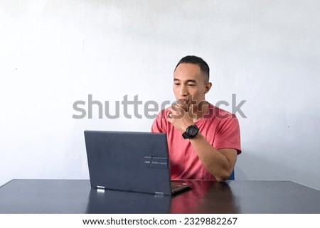 Wow face, smile, and happy of Young Asian man shocked and confuse what he see in the laptop on the table. Indonesia Man wear red shirt Isolated grey background.