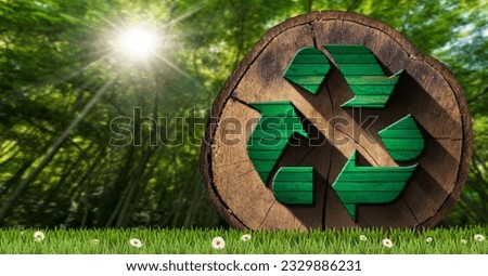 Sustainable Resources and Zero Waste concept. Cross section of a tree trunk with a wooden recycle symbol on a green meadow with daisy flowers and a green forest on background. Royalty-Free Stock Photo #2329886231