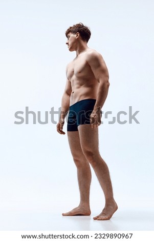 Full-length image of young man with muscular body posing shirtless in underwear against grey studio background. Strength. Concept of man's beauty, sportive and healthy lifestyle, athletic body Royalty-Free Stock Photo #2329890967