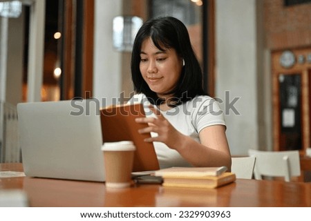 A pretty Asian woman in casual clothes reading a book while emote working at a coffee shop. remote working, freelance, digital nomad
