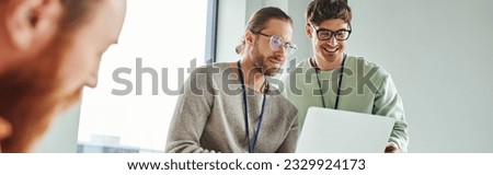 creative architects in casual clothes and eyeglasses looking at laptop near colleague working on blurred foreground, collaboration, innovative ideas, modern coworking office, banner