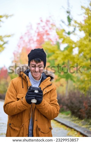 Smiling young man holding a hot cup of coffee on a cold autumn day.