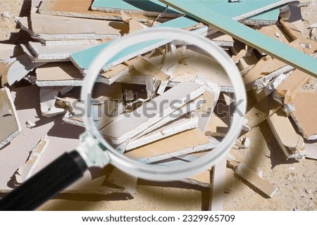 Demolished plasterboard wall, made of plaster and cardboard, with fragments of material and dust in a construction site - focus concept with magnifying glass