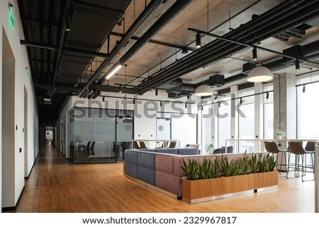 spacious and contemporary office lounge with soft and comfortable couch, large windows, high chairs and green plants, workspace organization concept Royalty-Free Stock Photo #2329967817