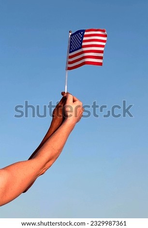 The two hand of a dark-skinned and white-skinned man holds the flag of America against the blue sky.the concept of national unity and patriotism, flag day, independence day of america