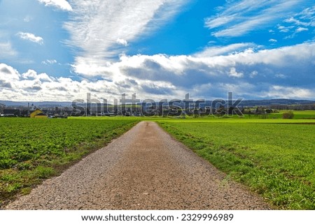 A landscape with clouds and a road to a village in a field
