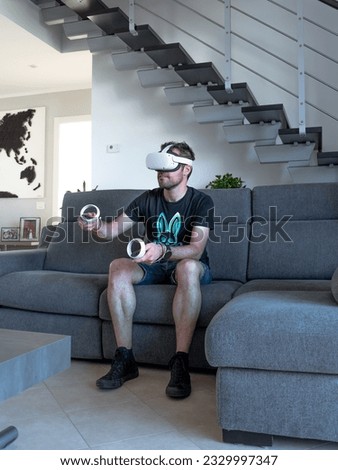 Young man sitting on sofa in flat playing games and having fun while wearing vr visor, technology