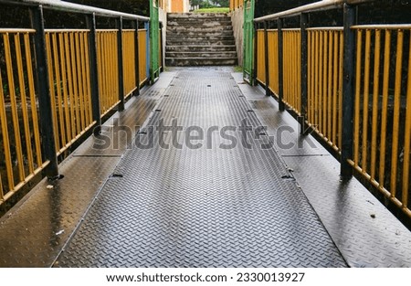 Metal walkway in the park on a rainy day with yellow railing