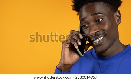 Communication concept. Closeup of smiling happy handsome young black man wearing blue sweater talking on phone, enjoying conversation, looking at copy space, isolated on yellow background, panorama