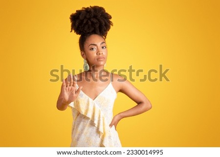 Serious strict confident millennial african american woman holding out her hand to camera, make no taking pictures sign, isolated on yellow background, studio. Stop gesture, no, ad and offer