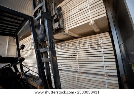 A diesel forklift loads freshly sawn pine logs, girders, bars, beams, bars, boards into a drying chamber. Industrial technology of wood production. Royalty-Free Stock Photo #2330038411