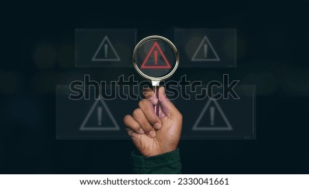 Man hand holding magnifier glass with red triangle caution warning sign for notification error. Notification error and maintenance, Programmer with hacker attacks, cyber crime and security.