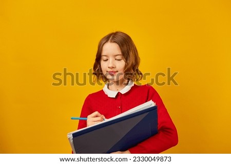 Thoughtful School teenage girl holding pen and write on notebook on yellow studio background, back to school concept