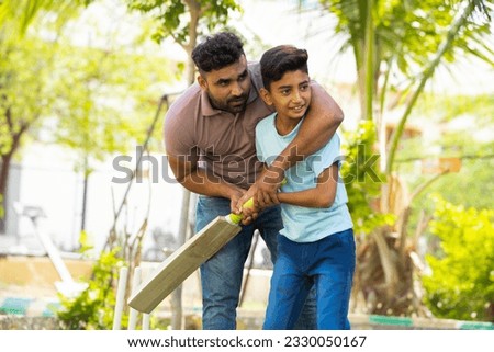 indian father teaching his son to playing cricket game at park - concept of Shared passion, family bonding and fatherhood Royalty-Free Stock Photo #2330050167