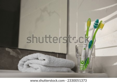 Colorful toothbrushes in glass holder and terry towel on table indoors