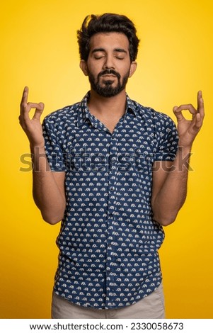 Keep calm down, relax, inner balance. Young indian man breathes deeply with mudra gesture, eyes closed, meditating with concentrated thoughts, peaceful mind. Hindu guy isolated on yellow background