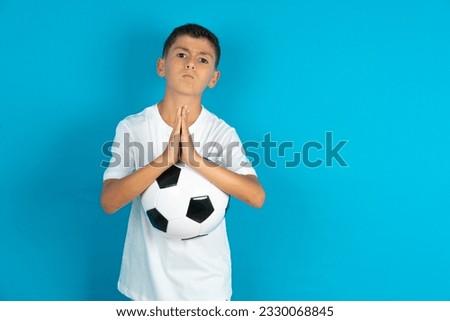 Positive Little hispanic boy wearing white T-shirt smiles happily, glad to receive pleasant news from interlocutor, keeps palms together, People emotions concept. Royalty-Free Stock Photo #2330068845