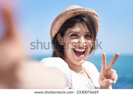Young hispanic woman tourist smiling confident make selfie by camera at seaside