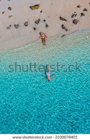 a couple swimming in the ocean of Koh Kradan Island with a white tropical beach and turqouse colored ocean. men and women in a blue ocean seen from above with a drone