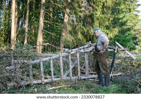 The storm did a great job, the high seat couldn't withstand the gusts and tipped over. The hunter looks at the damage.  Royalty-Free Stock Photo #2330078827