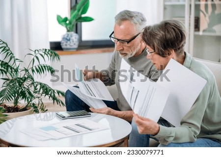 Elderly couple checking documents with tax and internal bills, making payments and discussing budget. Family calculating funds for purchase new home or car. Royalty-Free Stock Photo #2330079771