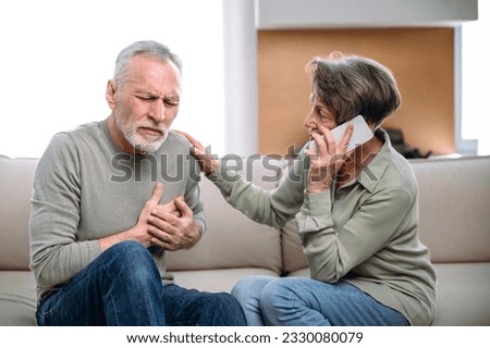 Elderly husband holding hand on chest, having heart attack, feeling unwell. Worried wife supporting partner call 911. Symptoms of myocardial infarction. Ambulance and immediate emergency help Royalty-Free Stock Photo #2330080079