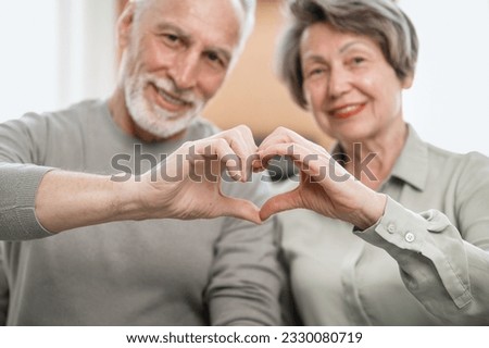 Love sign with hands. Mature couple showing heart gesture, smiling and looking at camera. Happy married people enjoying free time together. Concept of healthcare at retirement