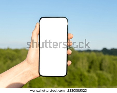 Hand holding mobile phone mockup over nature background, forest and sky.