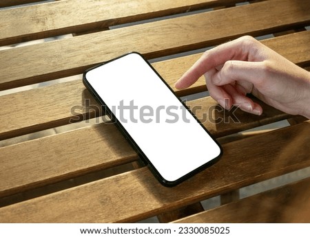 Hand using mobile phone mockup, smartphone screen mock up on sunny wooden desk.