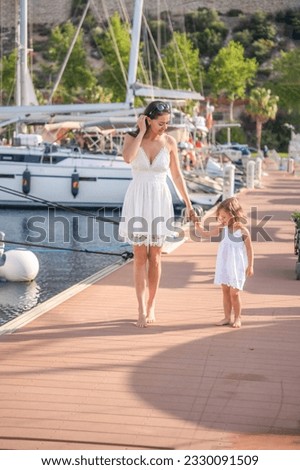 Happy mother and daughter child having fun on luxury yachts on background in marina. Family travel, lifestyle, vacation concept. High quality photo