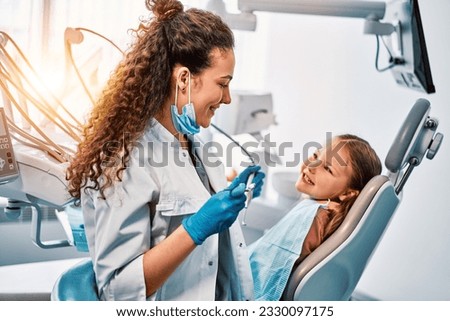 A female dentist doctor talks to a small patient, the child shows her teeth and sits in the dental chair.Sunlight. Royalty-Free Stock Photo #2330097175