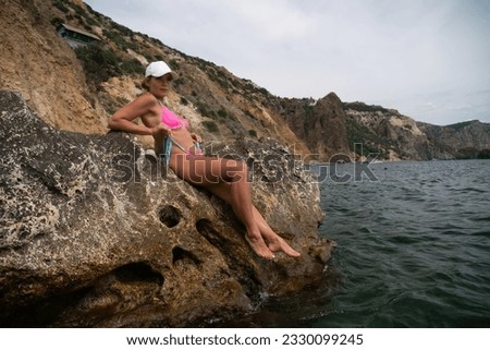 Woman travel sea. Pink bikini tourist captures sea memory, posing on beach amidst volcanic mountains for travel adventure. Happy woman enjoys outdoor photography.