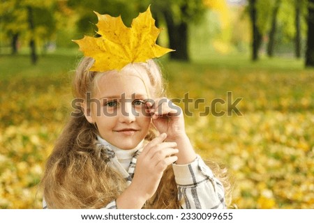Little blonde girl holding an autumn leaf in her hands and looking at the camera. Horizontal photo